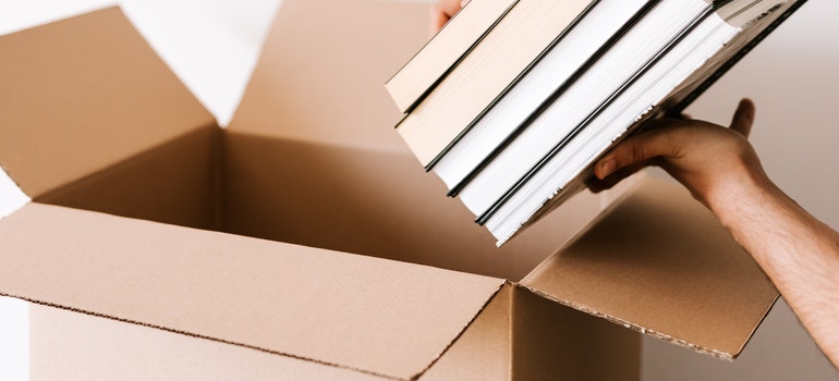 Person packing stacks of books in carton box