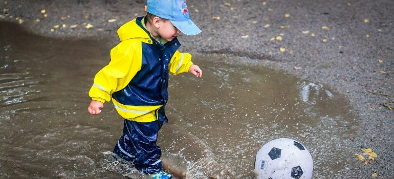 A boy playing with a ball while jumping in a puddle