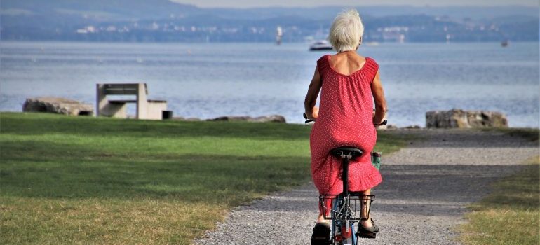 An older woman is riding a bicycle in a park next to the sea, representing activities one can enjoy if one retires in South Point