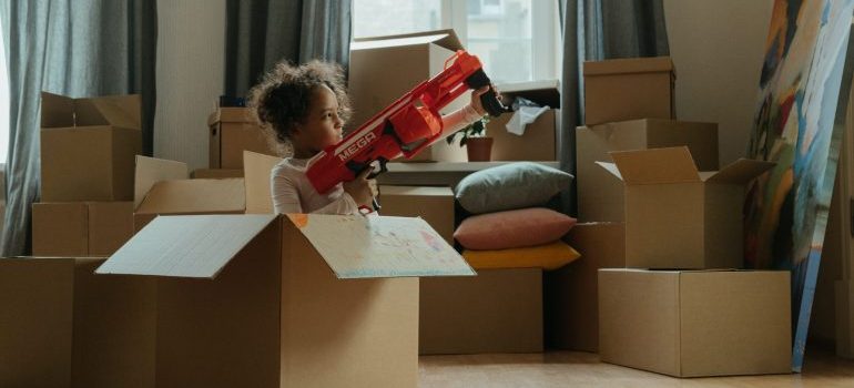 A girl playing with a plastic toy in a cardboard box representing keeping your kids entertained while moving to Coconut Grove