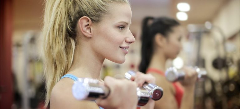 Two girls with ponytails are exercising in the gym with hand weights. 