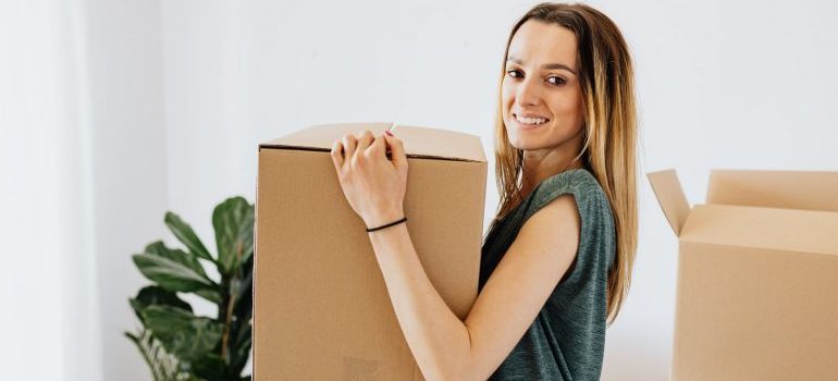 Cheerful woman carrying the box. Relocate with ease with local movers Fort Lauderdale