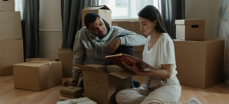 a couple sitting on a floor surrounded by moving boxes looking at a photo album
