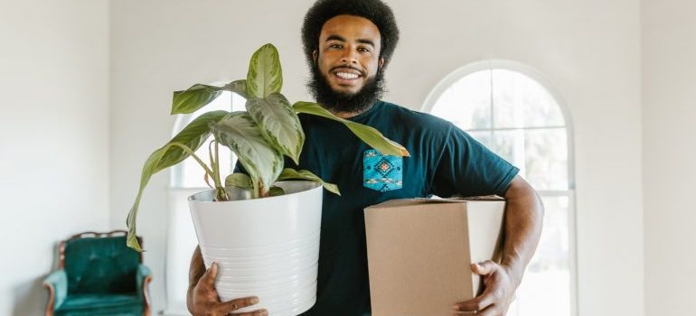A movers carrying a plant and small moving box