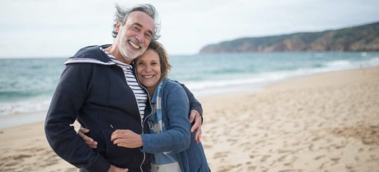 an elderly couple hugging and smiling at the beach