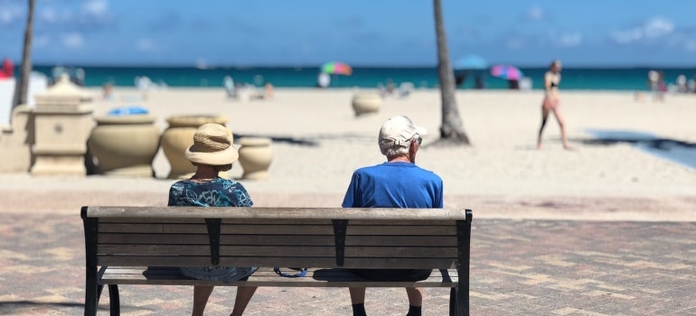 An elderly couple sitting on a bench near the sea