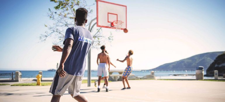 Friends playing basketball outdoors and thinking about reasons to move to Miami this spring.